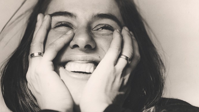 Fotografie einer jungen, lachende Frau mit den Händen an den Wangen.